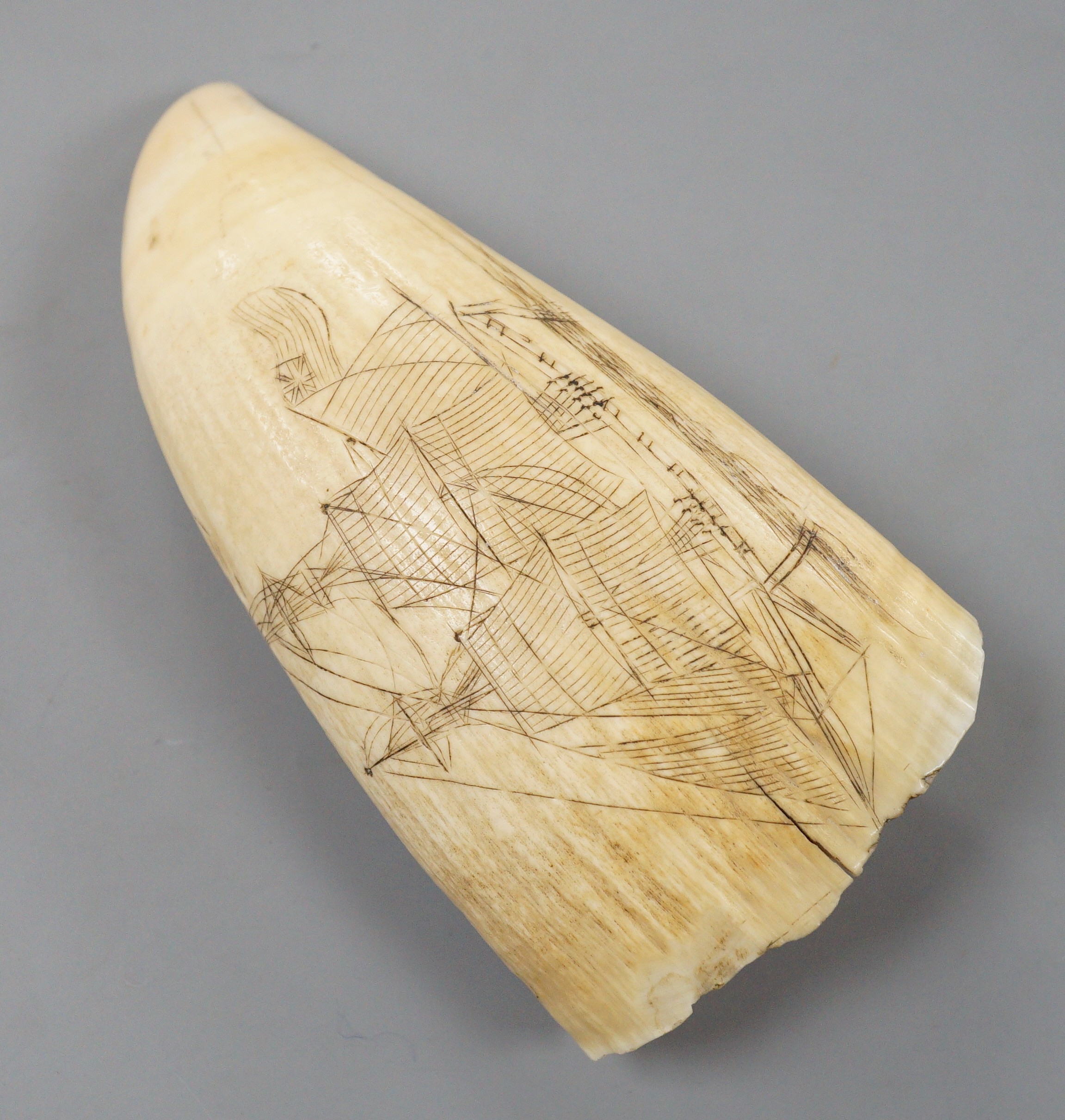 A 19th century worked scrimshaw sperm whale tooth depicting a period mother and child, and British sailing ship to reverse, 14cm long